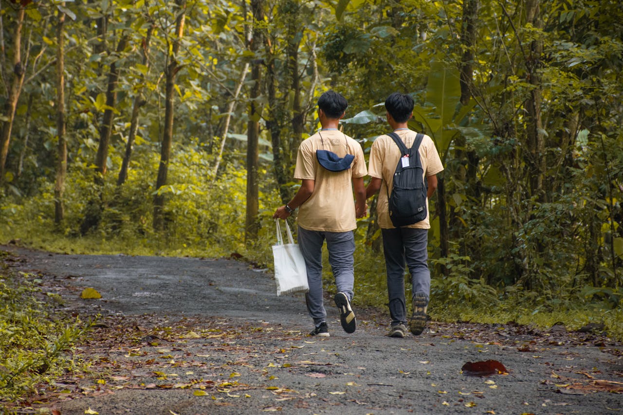 Two male friends walking along a forest path in Indonesia during their hike.